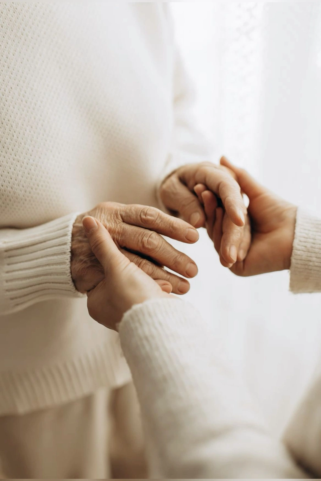An older adult's hands held gently by a caregiver